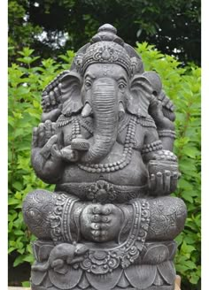 an elephant statue sitting on top of a wooden table in front of some bushes and trees