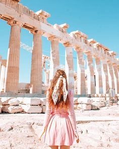 a woman standing in front of the ruins of an ancient temple with her hair blowing in the wind