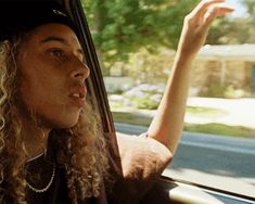 a woman with curly hair sitting in a car and pointing to the side while wearing a hat