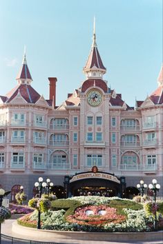 a large pink building with a clock on it's face and flowers in the foreground