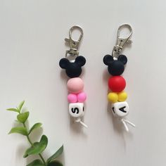 two mickey mouse keychains with different colors and numbers on them next to a plant