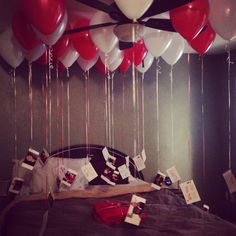 red and white balloons are hanging from the ceiling above a bed in a room that has been decorated for valentine's day