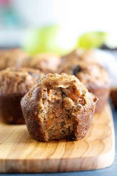 some muffins are sitting on a wooden cutting board with apples in the background