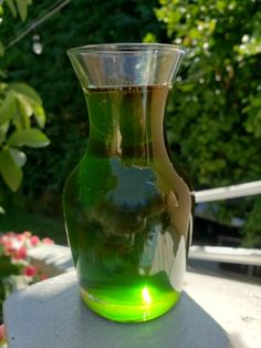 a green glass vase sitting on top of a white table in front of some flowers