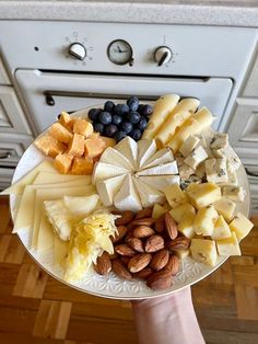 a person holding a plate with different types of cheeses, nuts and blueberries