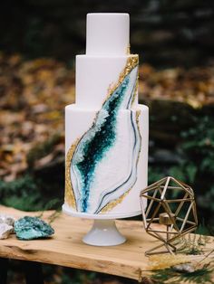 a white and gold wedding cake sitting on top of a wooden table in the woods