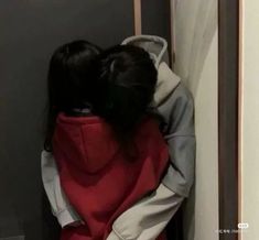 two people hugging each other in front of a door with their backs to the wall