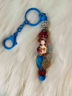 a keychain with a little mermaid on it sitting on a furry surface next to a pair of scissors