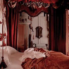 an old fashioned bedroom with red drapes on the ceiling and curtains hanging over the bed