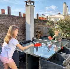 two children playing ping pong on an outdoor patio