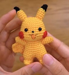 a hand holding a small yellow crocheted stuffed animal with black ears and eyes