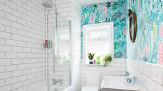 a white toilet sitting next to a bath tub under a bathroom window covered in blue and green wallpaper