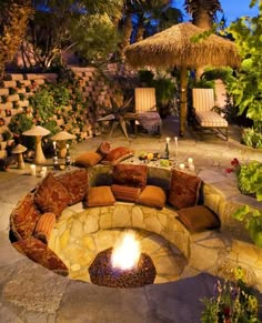 an outdoor fire pit surrounded by seating and trees at night with thatched umbrella in the background