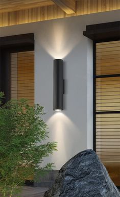 a modern outdoor wall light on the side of a house with rocks in front of it