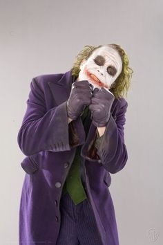 a man dressed as the joker is holding his hands up to his face while standing in front of a white background