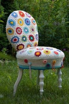 a crocheted chair sitting on top of a grass covered field next to flowers