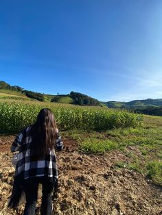 a woman standing on top of a dirt field next to a lush green field and blue sky