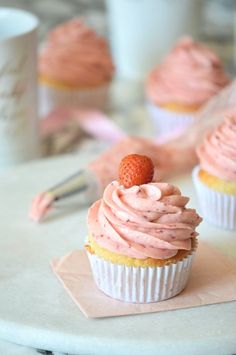 two cupcakes with pink frosting and a strawberry on top are sitting on a napkin