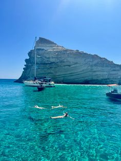 two people snorng in the clear blue water near an island with a sailboat