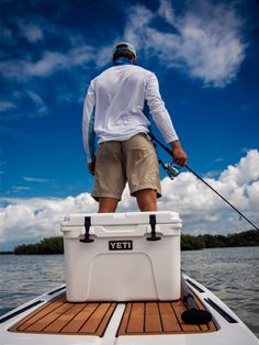 a man standing on the back of a boat holding a fishing rod and ice chest