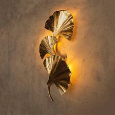 two gold leaf shaped sconces on the wall next to each other with light coming from them