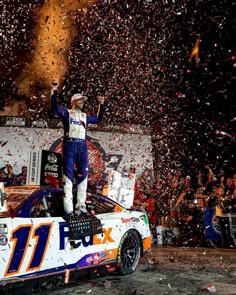 a man standing on top of a race car with confetti in the air