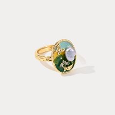 Introducing the enchanting Pearl Garden Ring, a masterful fusion of nature and elegance. This exquisite piece features a captivating garden motif, meticulously crafted in 18K gold-plated brass, offering a luxurious touch that exudes sophistication. The ring's centerpiece is adorned with a lustrous pearl, nestled amid a vibrant enamel backdrop that seamlessly blends shades of green and yellow, reminiscent of a serene garden bathed in sunlight. A delicate butterfly hovers above, sparkling with cry Elegant Green Enamel Ring As A Gift, Elegant Handmade Enamel Wedding Ring, Handmade Elegant Enamel Wedding Ring, Elegant Floral Enamel Ring For Wedding, Nature-inspired Green Flower Ring As A Gift, Elegant Green Oval Flower Ring, Elegant Green Pearl Ring For Gift, Elegant Green Enamel Ring Gift, Elegant Flower Enamel Ring For Wedding