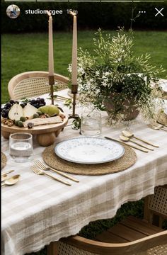 a table set with plates, silverware and candles on it in the middle of a yard