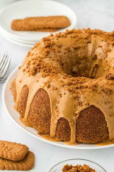 a bundt cake with frosting on a white plate next to cookies and forks