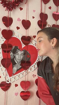 a woman standing in front of a wall with hearts hanging from it's sides