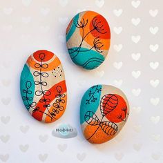 three painted rocks sitting next to each other on a white surface with hearts in the background