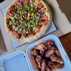 a pizza sitting on top of a table next to containers of chicken wings and veggies