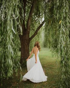 a woman in a wedding dress walking under a tree