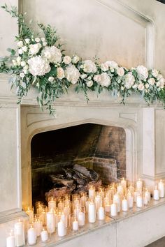 candles are lined up in front of a fireplace with flowers and greenery on it