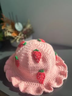 a crocheted pink hat with strawberries on the brim sits on a table