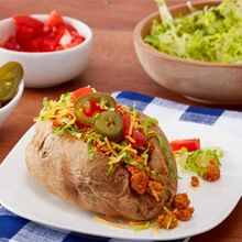 a baked potato covered in toppings sits on a plate next to bowls of salad