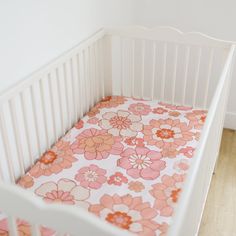 a white crib with pink and orange flowers on the bed sheet in front of it