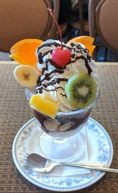 an ice cream sundae with fruit and chocolate toppings on a white saucer