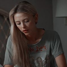 a woman with long hair sitting on a bed looking down at her cell phone and reading