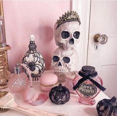 an assortment of perfumes and skull statues on a table in front of a pink wall