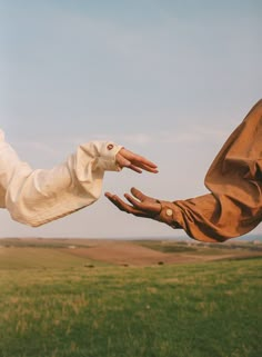 two hands reaching out towards each other in front of a green field and blue sky