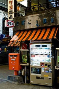 a vending machine sitting next to a building with an orange and white awning