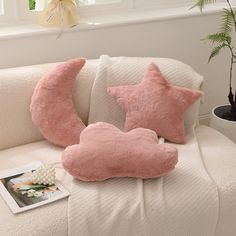 two pink stars and a crescent pillow on a white couch next to a potted plant