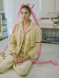 a woman sitting on the floor with a pink ribbon around her head and wearing a yellow jacket