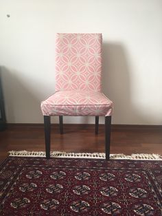 a pink chair sitting on top of a wooden floor next to a rug and wall