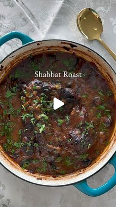 a pot filled with meat and garnish next to a spoon on top of a table