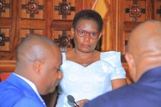 a woman in a white dress sitting at a table with two other people looking on