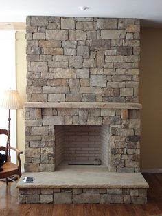 a living room with a stone fireplace in the center and wood flooring on the other side