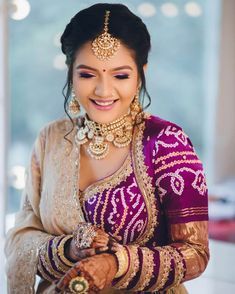 a woman in a purple and gold bridal outfit smiles as she holds her hands together