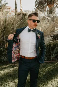 a man in a suit and bow tie is holding his jacket over his shoulder while standing on the grass